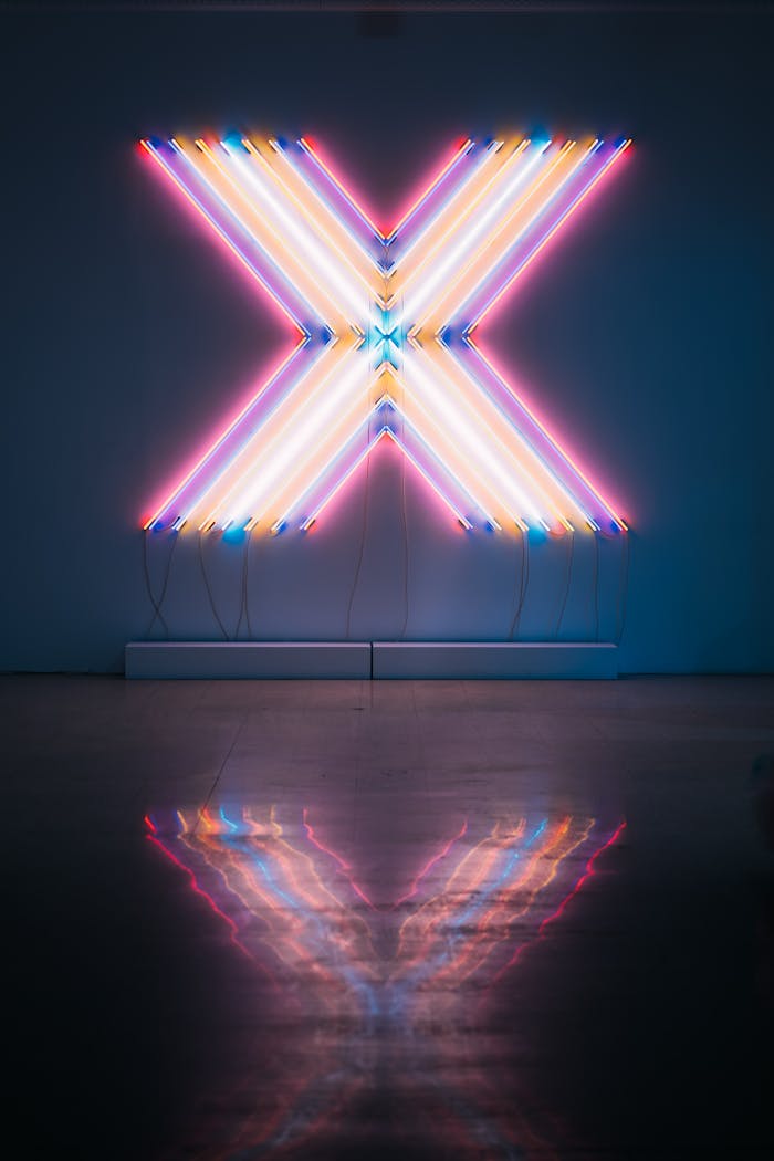 Vibrant neon X sign with colorful reflections on a dark floor background.